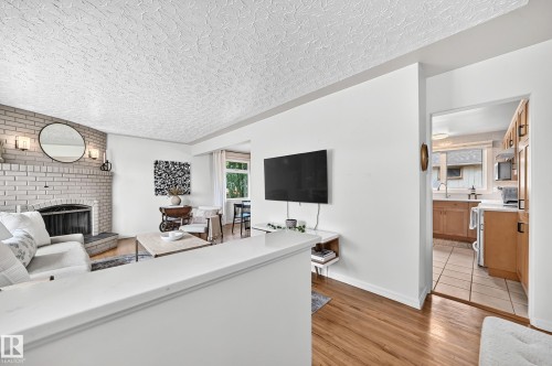 Living area featuring a painted brick fireplace with a mantel, wood-finish flooring, and white walls - 16406 87A Avenue Nw, Edmonton, AB - Indoor