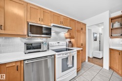 Light wood-finish cabinetry, white countertops, subway tile backsplash, white electric range, and stainless steel dishwasher - 