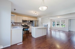 Wood-finish flooring throughout, kitchen with stainless steel appliances, central island with solid surface countertop, white cabinetry, and a fireplace with a mantel - 