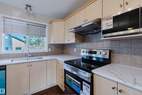 Contemporary kitchen featuring a stainless steel electric range, over-range microwave, and a double basin sink with a gooseneck faucet - 5887 Sutter Place Nw, Edmonton, AB - Indoor Photo Showing Kitchen With Double Sink
