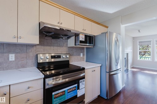 Kitchen featuring white cabinetry, stainless steel appliances, stone-look countertops, and a tiled backsplash - 5887 Sutter Place Nw, Edmonton, AB - Indoor Photo Showing Kitchen With Stainless Steel Kitchen
