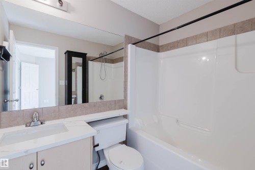 Vanity with integrated sink and chrome faucet, large mirror, tile backsplash, toilet, and a white tub/shower combination with a black shower rod - 5887 Sutter Place Nw, Edmonton, AB - Indoor Photo Showing Bathroom