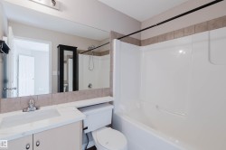 Vanity with integrated sink and chrome faucet, large mirror, tile backsplash, toilet, and a white tub/shower combination with a black shower rod - 