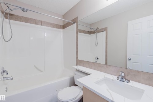 Bathroom featuring a combination shower and tub, tile surround, integrated vanity sink, and a large wall-mounted mirror - 5887 Sutter Place Nw, Edmonton, AB - Indoor Photo Showing Bathroom