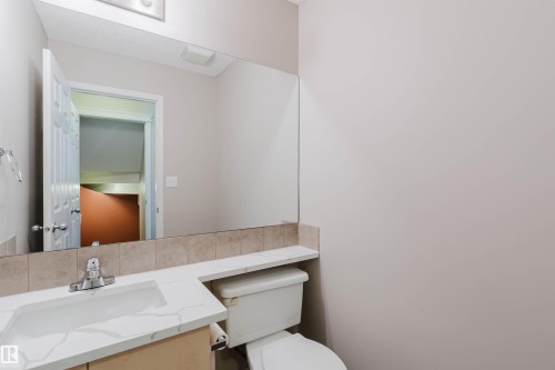 Full-width vanity mirror, integrated sink, light-toned wood-finish cabinetry, and tiled backsplash - 5887 Sutter Place Nw, Edmonton, AB - Indoor Photo Showing Bathroom