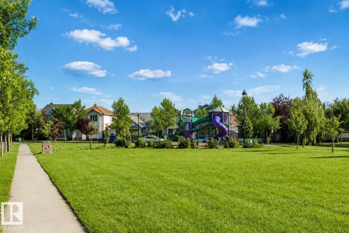 Expansive grassy area featuring a children's play structure, mature trees, and a paved walkway - 5887 Sutter Place Nw, Edmonton, AB - Outdoor