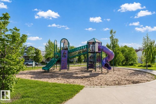 Outdoor playground featuring a multi-level structure with slides and a climbing wall, set within a sandy ground cover - 5887 Sutter Place Nw, Edmonton, AB - Outdoor