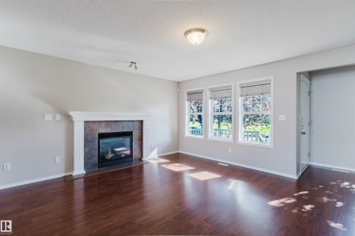 Living area with wood-finish flooring, a fireplace featuring a tile surround and white mantel, and a bank of three windows - 5887 Sutter Place Nw, Edmonton, AB - Indoor Photo Showing Living Room With Fireplace
