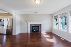 Hardwood-finish flooring, recessed fireplace with tile surround and mantel, multiple windows, stainless steel refrigerator, and built-in kitchen cabinetry - 