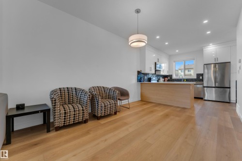Open-concept living space featuring wood-finish flooring, recessed lighting, a modern kitchen with white cabinetry, and stainless steel appliances - 3610 42 Avenue, Beaumont, AB - Indoor Photo Showing Kitchen