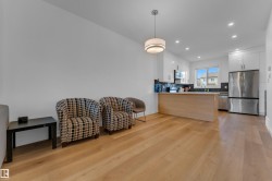 Open-concept living space featuring wood-finish flooring, recessed lighting, a modern kitchen with white cabinetry, and stainless steel appliances - 