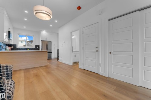 Wood-finish flooring throughout, white shaker-style cabinetry, stainless steel refrigerator, dark tiled backsplash, and recessed lighting - 3610 42 Avenue, Beaumont, AB - Indoor