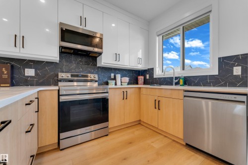 White upper cabinetry, wood-finish lower cabinetry, stainless steel appliances, patterned backsplash, and wood-finish flooring - 3610 42 Avenue, Beaumont, AB - Indoor Photo Showing Kitchen