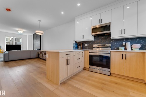 Modern kitchen with stainless steel appliances, light wood-finish cabinetry, white countertops, and a dark patterned backsplash - 3610 42 Avenue, Beaumont, AB - Indoor Photo Showing Kitchen