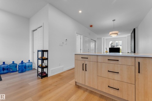 Contemporary kitchen island with light wood-finish cabinetry, black hardware, and a light-toned countertop - 3610 42 Avenue, Beaumont, AB - Indoor