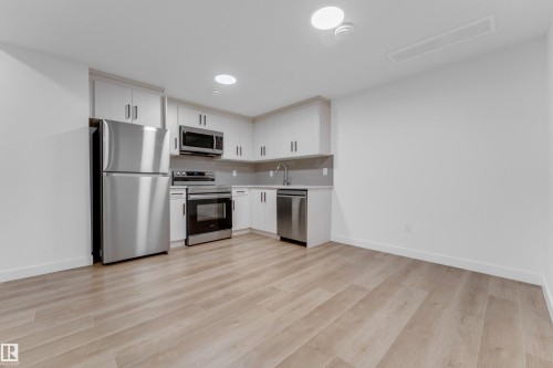 Contemporary kitchen featuring stainless steel appliances, light-toned cabinetry, and wood-finish flooring - 3610 42 Avenue, Beaumont, AB - Indoor Photo Showing Kitchen