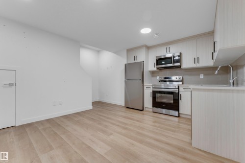 Modern kitchen with stainless steel appliances, light wood-finish cabinetry, light countertops, a tile backsplash, and wood-finish flooring - 3610 42 Avenue, Beaumont, AB - Indoor Photo Showing Kitchen