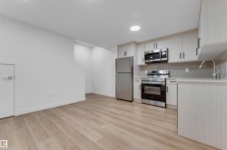 Modern kitchen with stainless steel appliances, light wood-finish cabinetry, light countertops, a tile backsplash, and wood-finish flooring - 