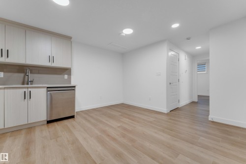 Neutral interior with wood-finish flooring, white walls, recessed lighting, and a compact kitchen area featuring light-toned cabinetry, a stainless steel dishwasher, and a sink with a chrome faucet - 3610 42 Avenue, Beaumont, AB - Indoor Photo Showing Kitchen