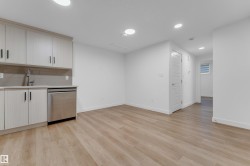 Neutral interior with wood-finish flooring, white walls, recessed lighting, and a compact kitchen area featuring light-toned cabinetry, a stainless steel dishwasher, and a sink with a chrome faucet - 