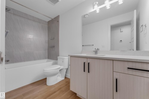 Modern bathroom featuring a wood-finish flooring, light grey vanity with a light-colored countertop, built-in sink, and a tiled shower-over-tub combination - 3610 42 Avenue, Beaumont, AB - Indoor Photo Showing Bathroom