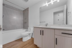 Modern bathroom featuring a wood-finish flooring, light grey vanity with a light-colored countertop, built-in sink, and a tiled shower-over-tub combination - 