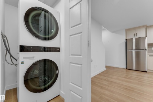 Stacked laundry appliances, stainless steel refrigerator, light wood-finish cabinetry, and wood-finish flooring - 3610 42 Avenue, Beaumont, AB - Indoor Photo Showing Laundry Room