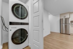 Stacked laundry appliances, stainless steel refrigerator, light wood-finish cabinetry, and wood-finish flooring - 