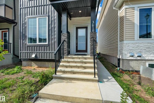 Front entry featuring concrete steps with black railings, a dark wood-finish door with frosted glass, and stone veneer accents - 3610 42 Avenue, Beaumont, AB - Outdoor