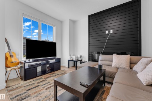 Living space featuring large windows, wood-finish flooring, and a contemporary fireplace with a dark paneled surround - 3610 42 Avenue, Beaumont, AB - Indoor Photo Showing Living Room