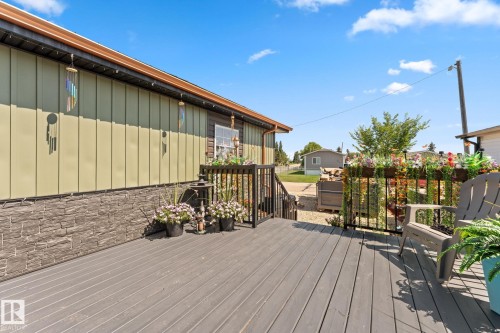 Expansive outdoor deck featuring dark composite decking, a black metal railing, and a window with a flower box - 5024 45A Street, Barrhead, AB - Outdoor With Deck Patio Veranda With Exterior