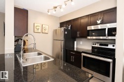 Kitchen featuring dark wood-finish cabinetry, stainless steel appliances, a double basin sink with a high-arch faucet, and dark countertops - 
