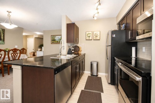 Kitchen with dark wood-finish cabinetry, stainless steel appliances, granite countertops, and light-toned flooring - #236 3315 James Mowatt Tr Sw, Edmonton, AB - Indoor Photo Showing Kitchen