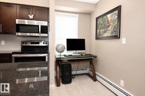 Dark wood cabinetry with stainless steel hardware, stainless steel microwave, stainless steel range, mosaic tile backsplash, and light wood-finish flooring - #236 3315 James Mowatt Tr Sw, Edmonton, AB - Indoor Photo Showing Kitchen