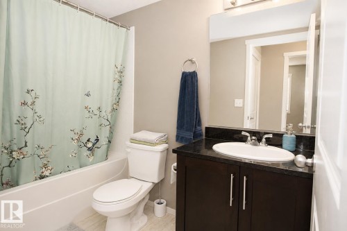 Dark wood-finish vanity with a built-in sink, dark countertop, and large wall-mounted mirror - #236 3315 James Mowatt Tr Sw, Edmonton, AB - Indoor Photo Showing Bathroom