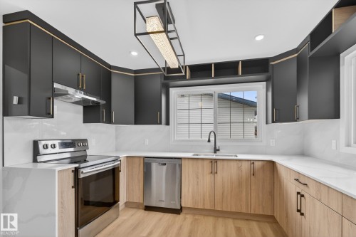 Modern kitchen featuring two-tone cabinetry, stainless steel appliances, white countertops, and a contemporary linear chandelier - 12936 132 Street Nw, Edmonton, AB 