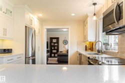 White shaker-style cabinetry with upper glass-front cabinets, stainless steel appliances, light-toned backsplash, and a contemporary pendant light fixture - 