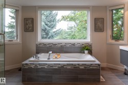 Built-in soaking tub with modern fixtures, surrounded by mosaic and wood-look tile - 