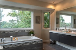 Built-in soaking tub with modern chrome fixtures, dual vessel sinks with integrated countertop, wall-mounted vanity with ample storage, tiled shower surround, and wood-finish flooring - 