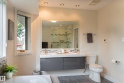 Recessed lighting, wood-finish flooring, dual floating vanity with integrated sinks, large mirrored wall, and a curved glass shower enclosure - 