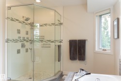 Glass-enclosed shower with multiple sprayers, a rainfall showerhead, and mosaic tile detailing - 
