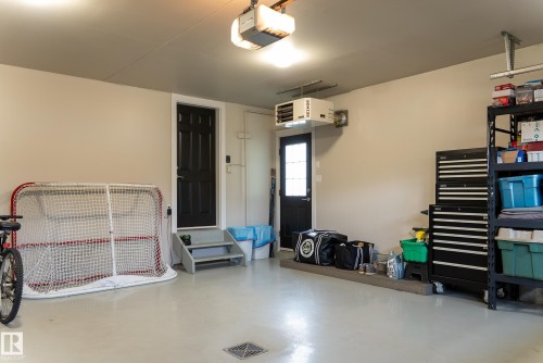 Attached garage featuring painted concrete flooring, two access doors, an overhead garage door opener, and a wall-mounted heating unit - 56 Highridge Way, Stony Plain, AB - Indoor Photo Showing Other Room
