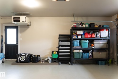 Spacious garage with light-colored flooring, wall-mounted heater, and a black exterior door featuring a window - 56 Highridge Way, Stony Plain, AB - Indoor