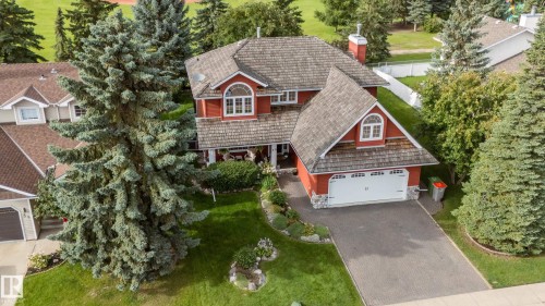 Red exterior siding with stone accents, shaker-style roof, arched dormer windows, attached two-car garage, and a paved driveway - 56 Highridge Way, Stony Plain, AB - Outdoor