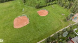 Expansive green space featuring two baseball diamonds, a playground structure, and mature trees - 