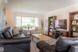 Spacious living room featuring multiple seating areas with dark leather furnishings, light wood-finish coffee table, and built-in entertainment center with shelving - 
