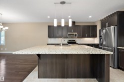 Kitchen featuring a large island with a speckled countertop, dark wood-finish cabinetry, stainless steel appliances, pendant lighting, and a tile backsplash - 