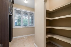 Expansive walk-in pantry featuring built-in shelving, tile flooring, and a large window with blinds - 