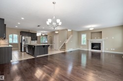 Expansive living area featuring rich wood-finish flooring, a contemporary fireplace with a decorative mantel, and an open layout to the kitchen - 