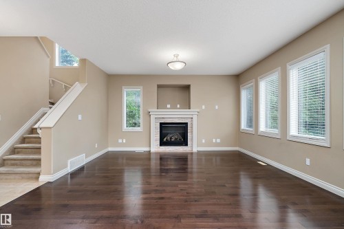 Spacious room featuring rich wood-finish flooring, a traditional fireplace with a white mantel and stone surround, and multiple windows with blinds - 11203 72 Avenue Nw, Edmonton, AB - Indoor With Fireplace